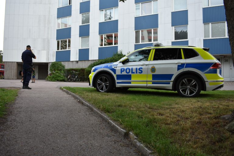 Parkerad polisbil och polisman framför hyreshus