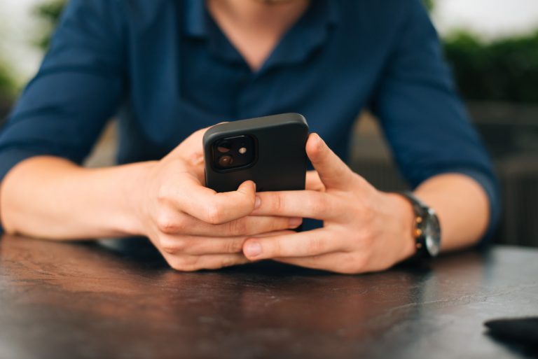 Man sitter vid bord med mobiltelefon i händerna