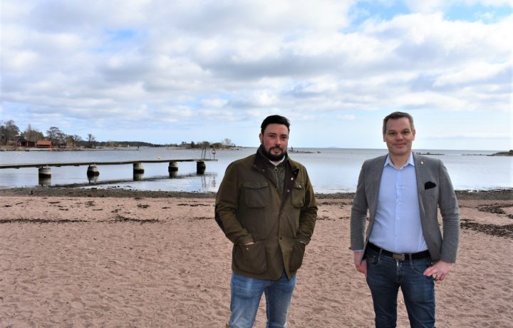 Lucas Lodge (M), kommunalråd i Oskarshamn, och Andreas Erlandsson (S), kommunstyrelsens ordförande i Oskarshamn, står på Havslätts badplats i Oskarshamn och tittar in i kameran