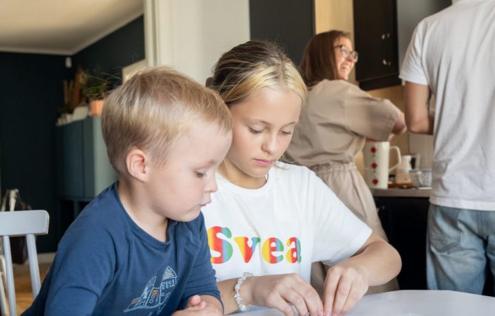 Barn som sitter i köket och föräldrar står vid bänken