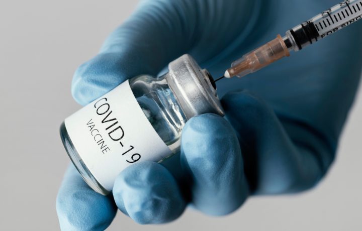 hand i skyddshandske som håller en burk Covid-19 vaccin som laddas i spruta