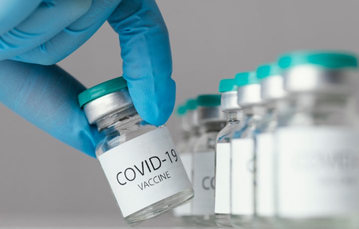 hand i skyddshandske som håller en burk Covid-19 vaccin