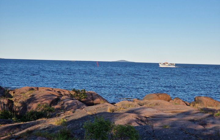 Ernemars klippor i Oskarshamn i förgrunden, Blå Jungfrun i bakgrunden, skärgårdsbåt i Kalmarsund.