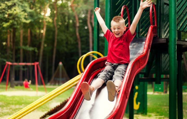 Liten kille som är glad och åker rutschkana