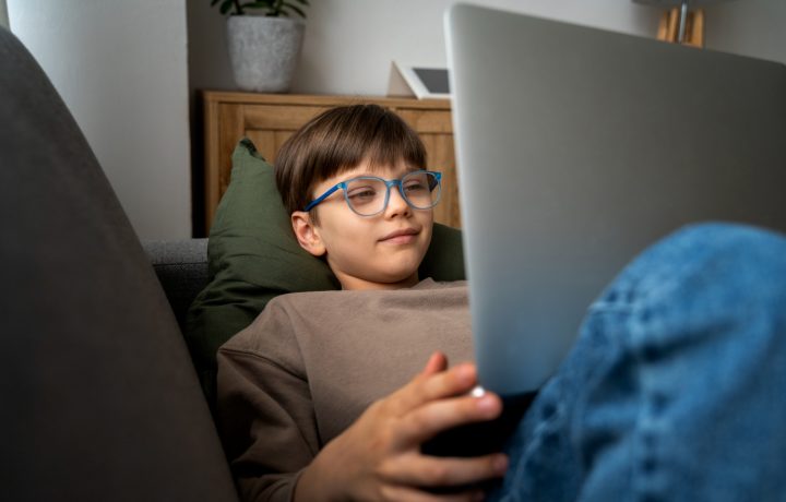 Pojke sitter i soffa med bärbar dator i knät