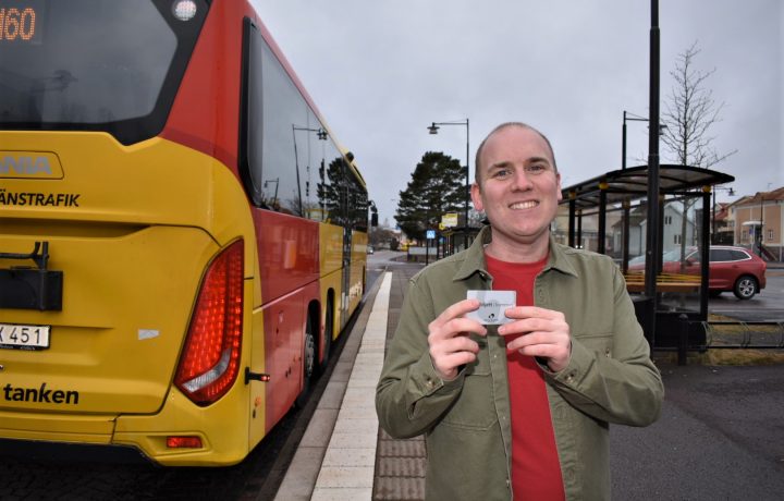 Anton Sejnehed (S) står med ett busskort i handen och en buss bredvid sig och tittar in i kameran