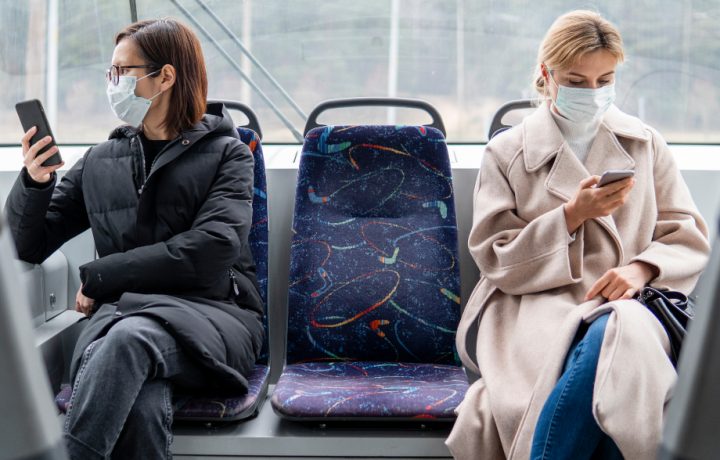 Två kvinnor med munskydd på buss som häller distans till varandra